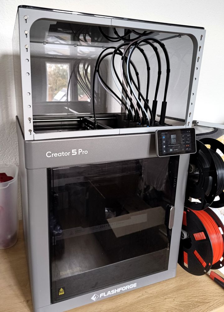 Geschlossener 3D-Drucker Creator 5 Pro mit Glastür und Aufsatz, daneben Filamentrollen.